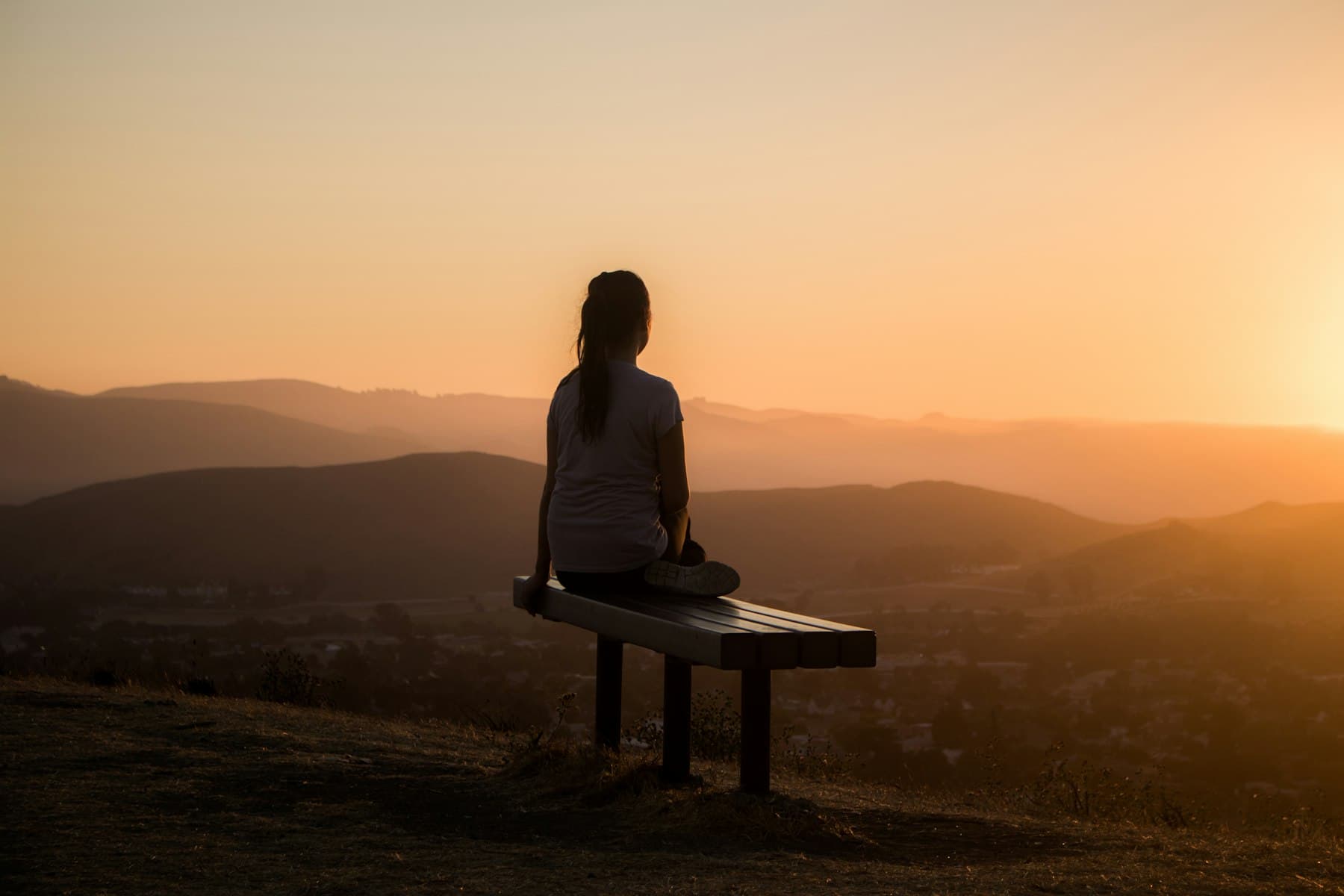 Person sitting on a bench overlooking a wide mountain landscape at golden hour