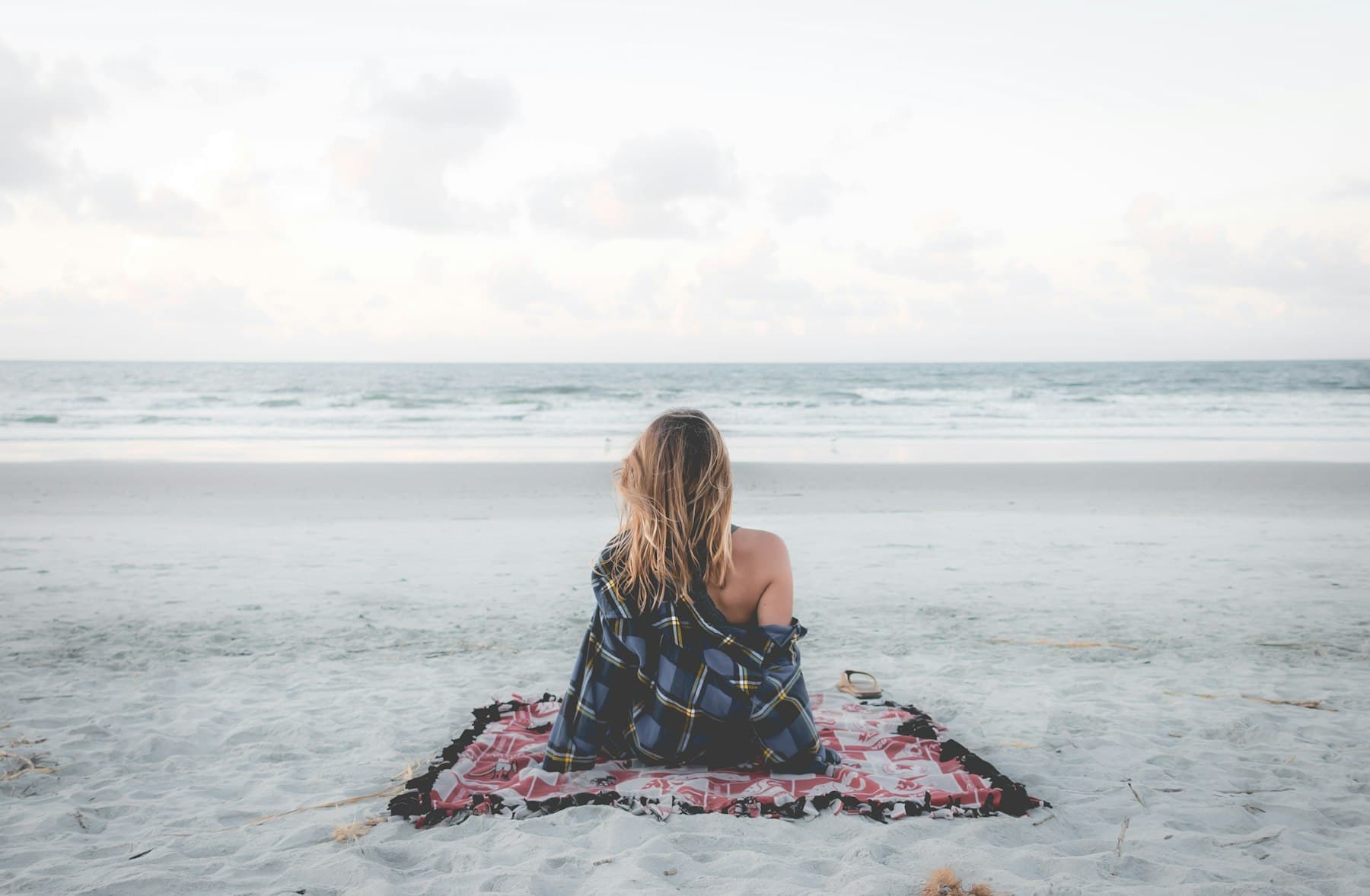 Woman sitting on a blanket by the shoreline at dusk