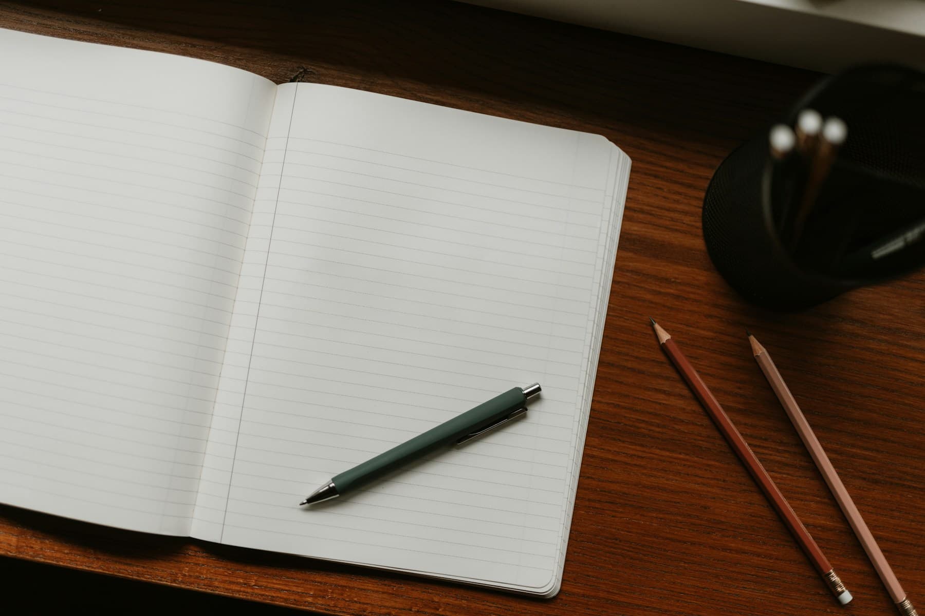 Open notebook and pen resting on a dark wooden desk