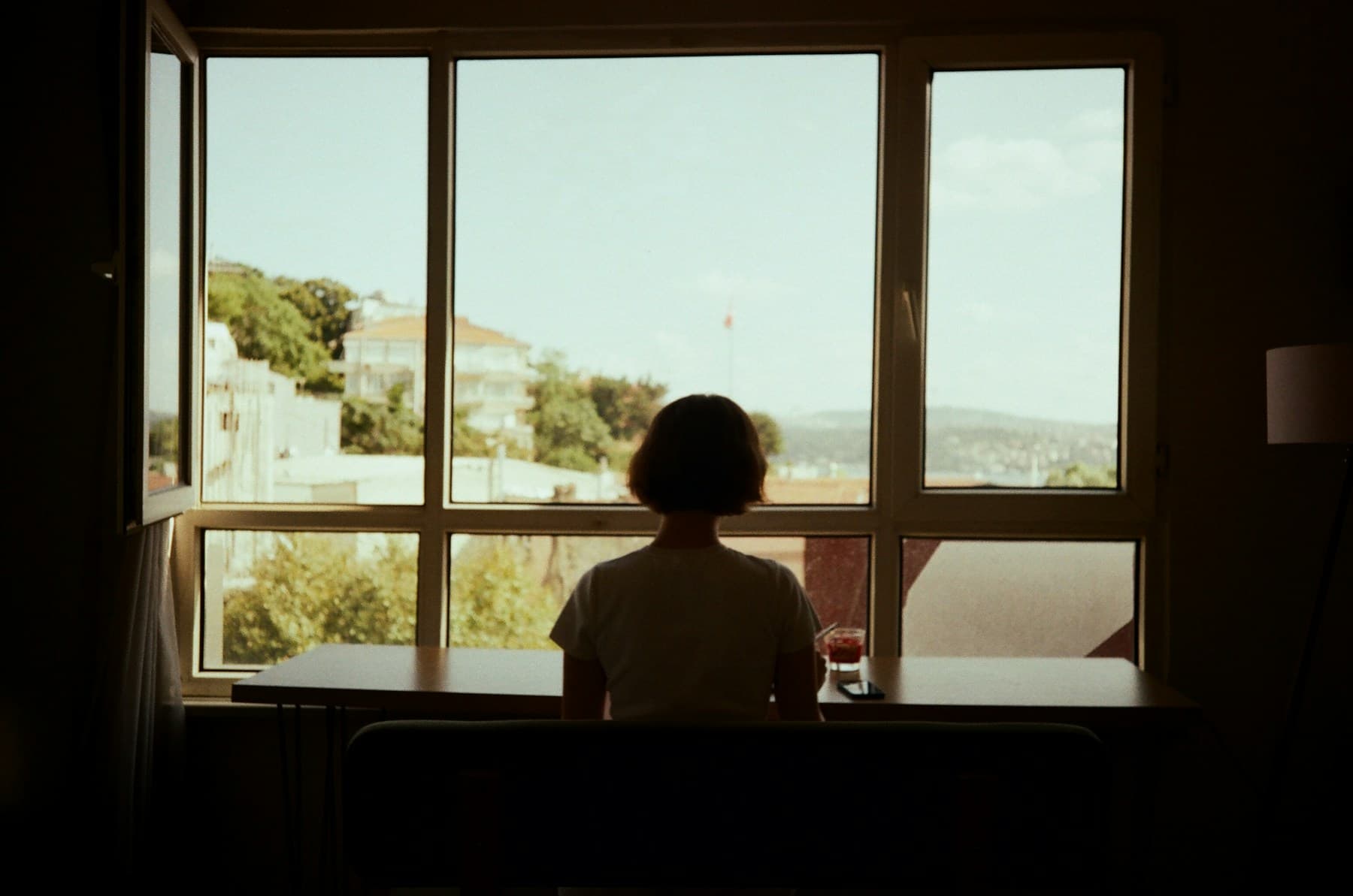 Person sitting at a table, looking out of an open window